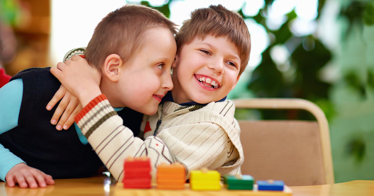 Two boys hugging at a table in a classroom.