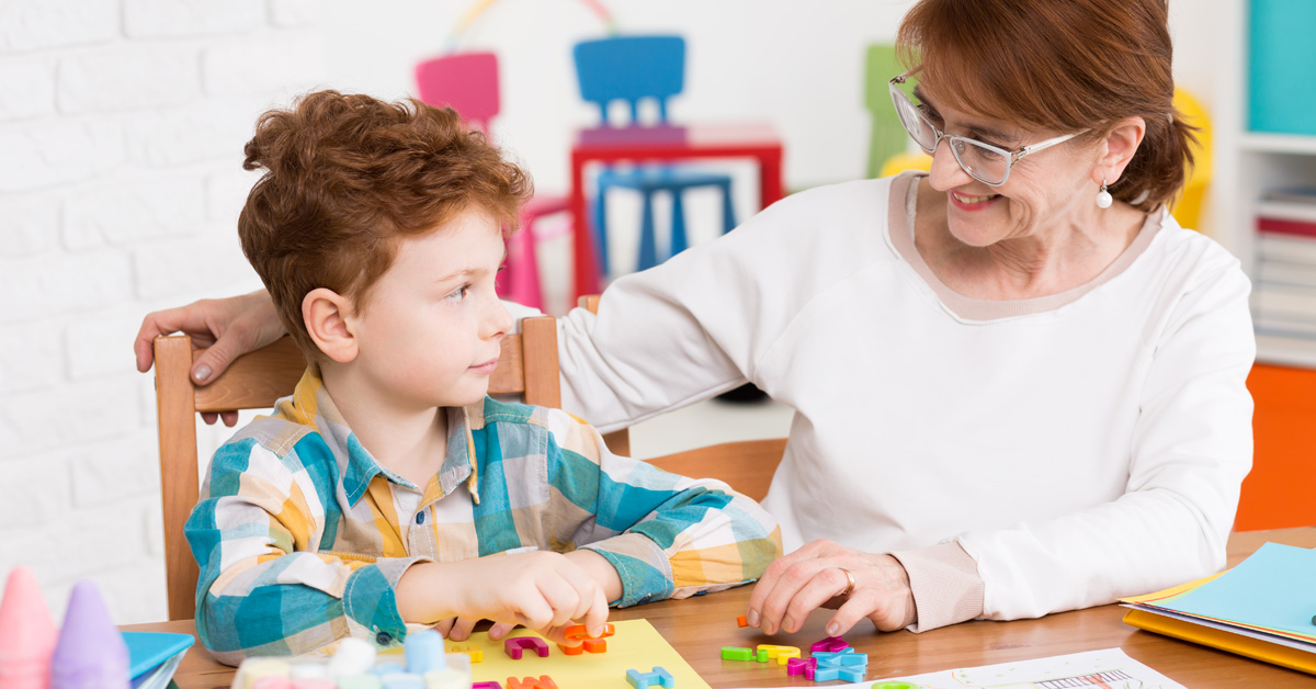 An older woman helping a young boy at a table.