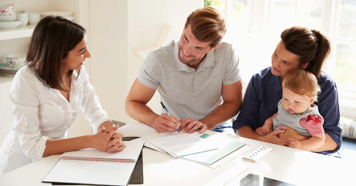 A family with a baby sitting at a table signing papers.