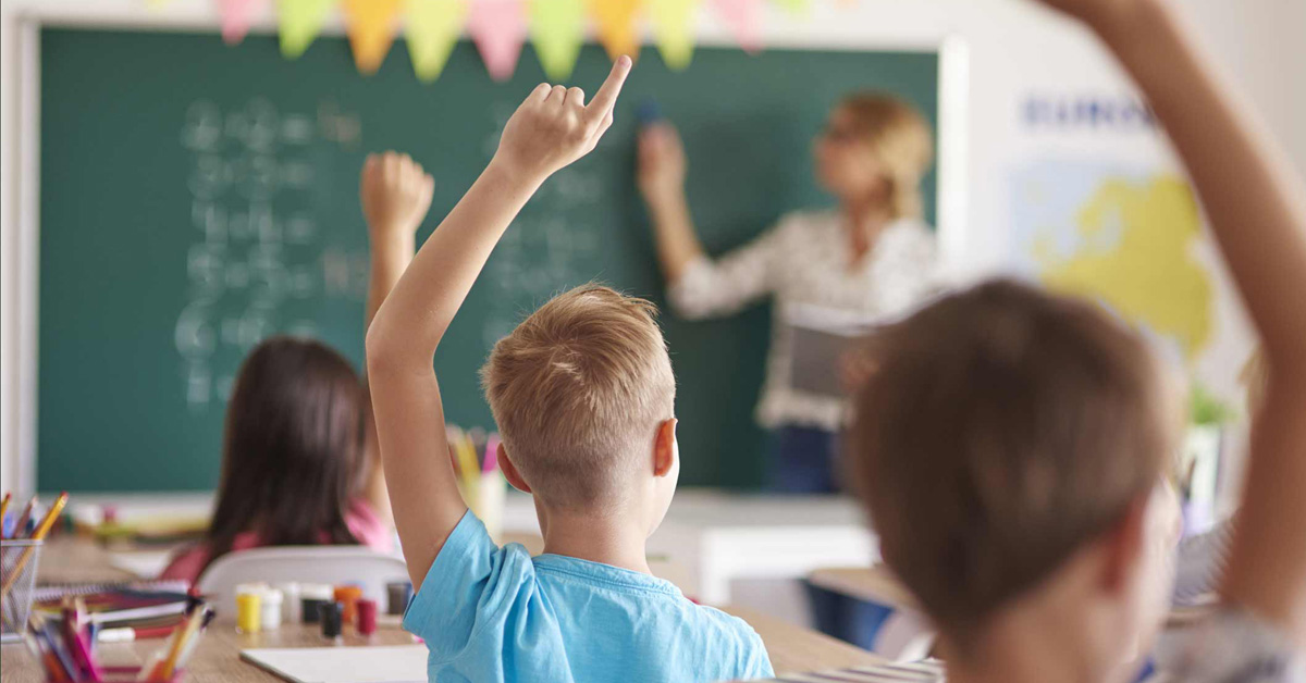 Children raising their hands in front of a blackboard.