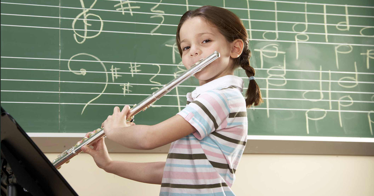 A young girl playing a flute in front of a blackboard.