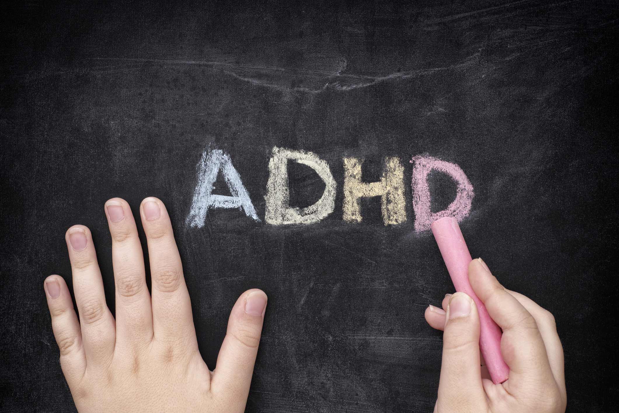 A hand writing the word adhd on a blackboard.