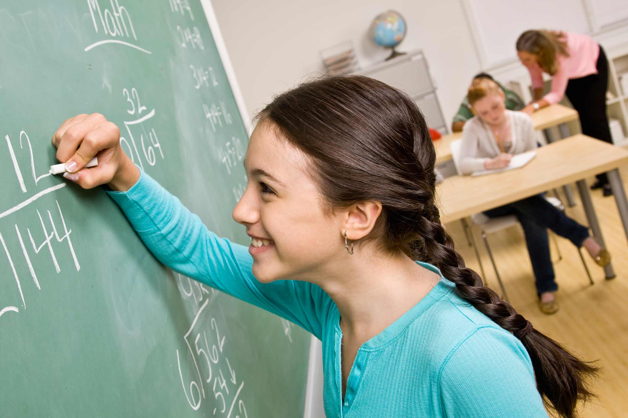 A girl is writing on a blackboard in a classroom.