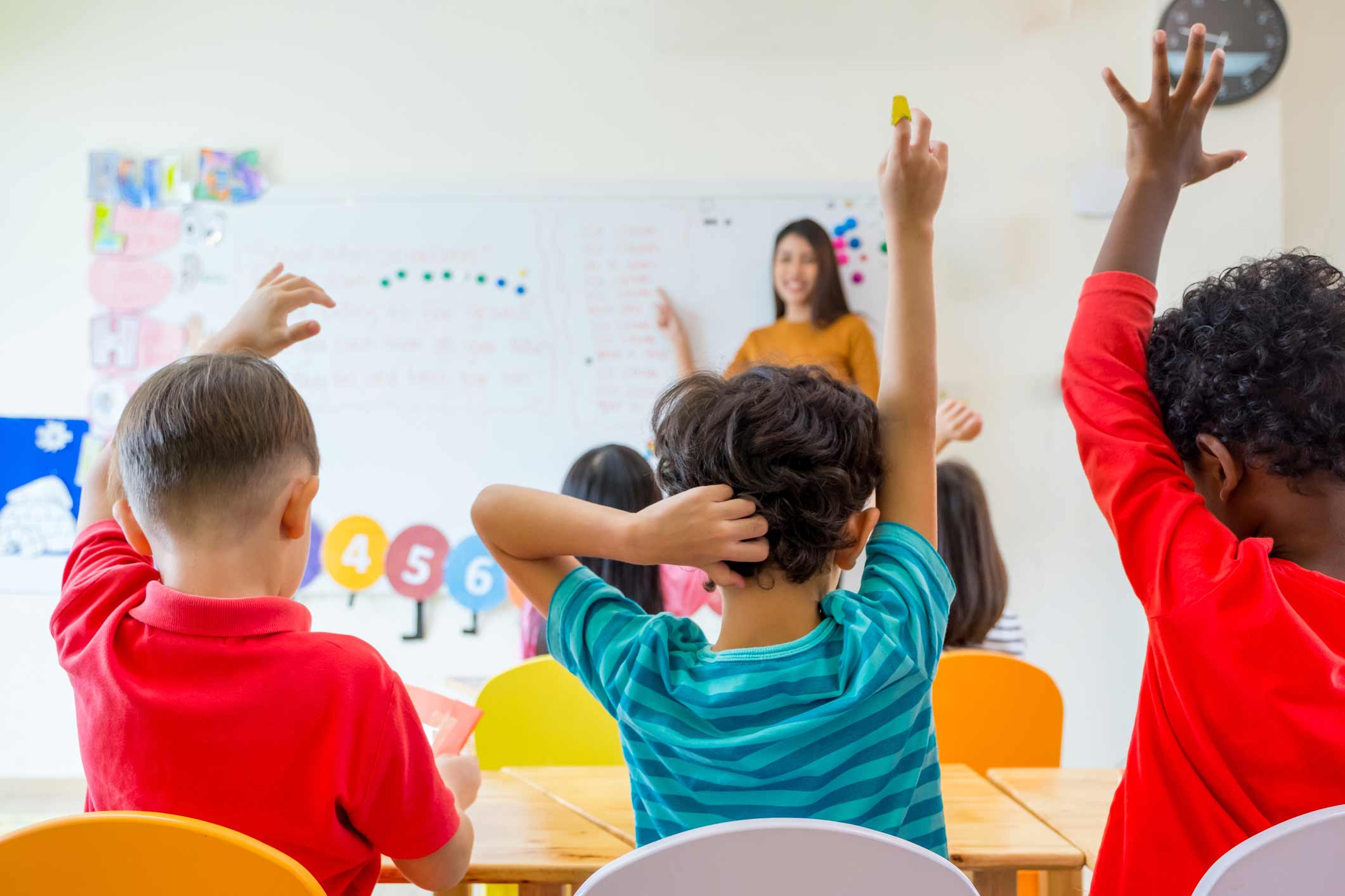 A group of children in a classroom raising their hands.