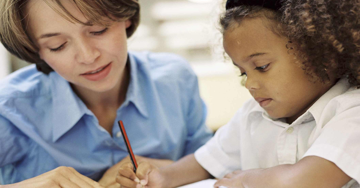 A woman helping a young girl with her homework.