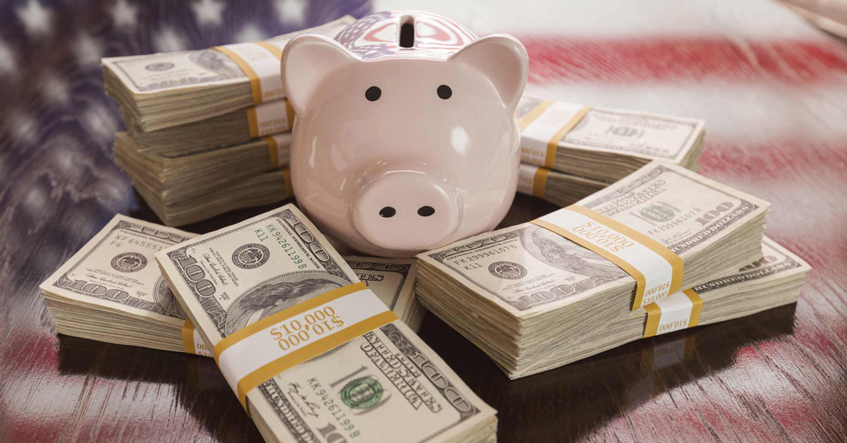 A piggy bank sits on top of piles of money with an american flag.