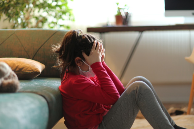 A young girl sitting on the floor with her hands on her head.