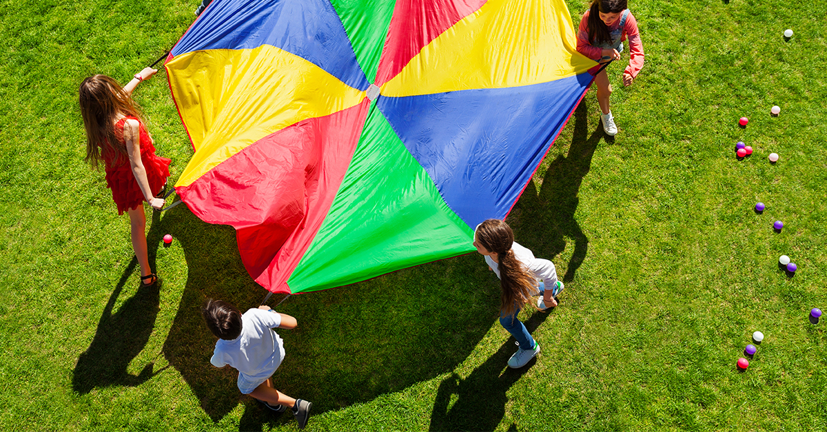A group of people playing with a colorful parachutist.