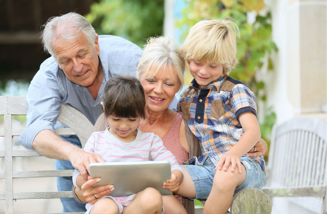 A family sitting on a bench looking at a tablet computer.