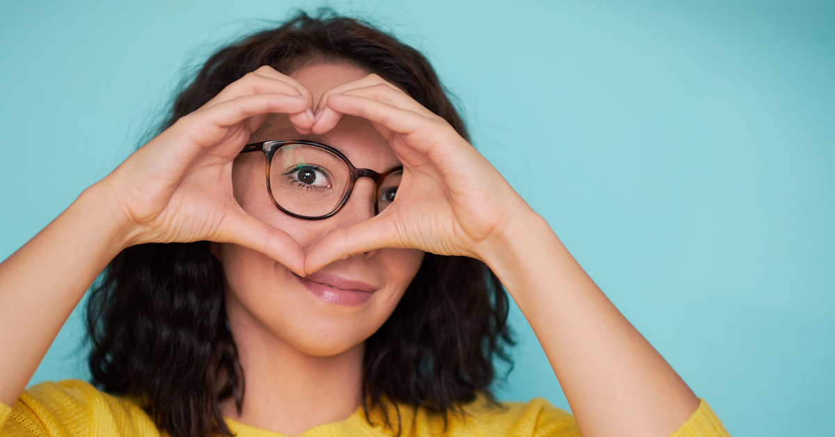 Young woman with glasses making a heart with her hands.