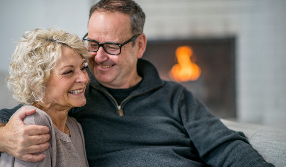 An older couple smiling in front of a cozy fireplace