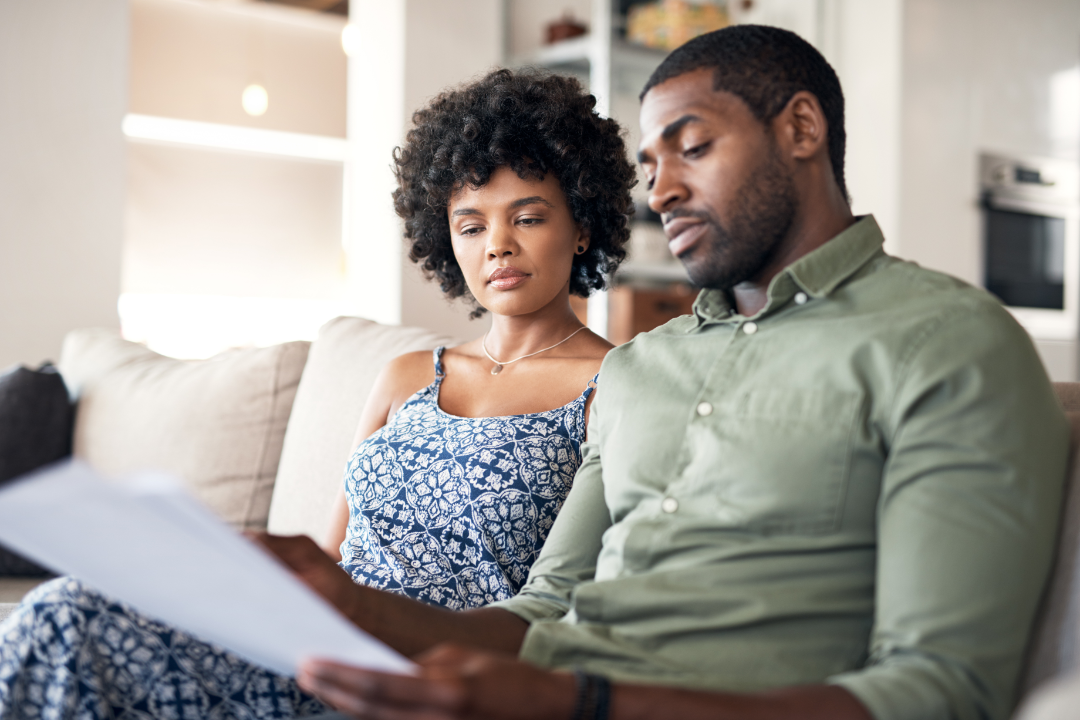 A man and woman sitting on a couch looking at papers.