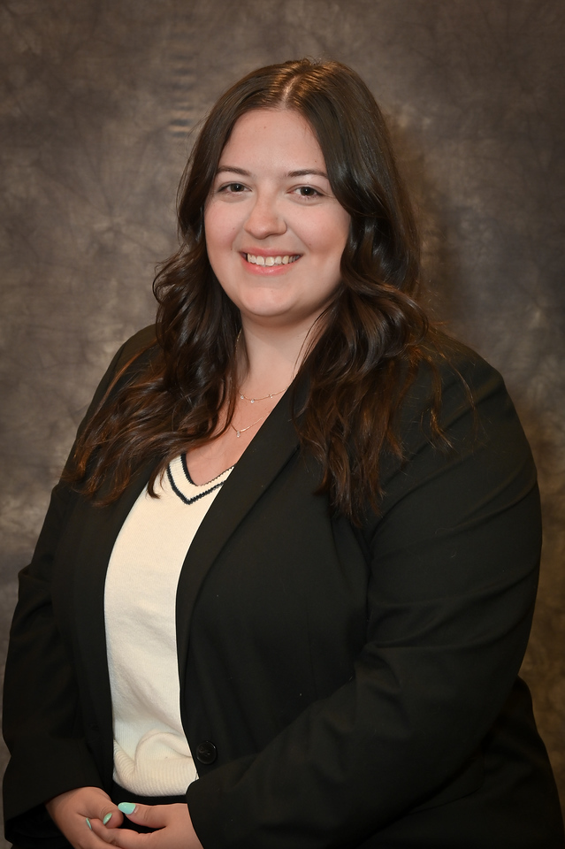 A woman in a business suit smiling in front of a window.