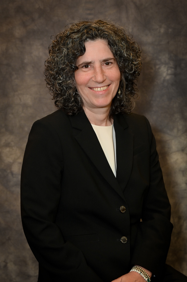 A woman in a business suit smiling in front of a window.